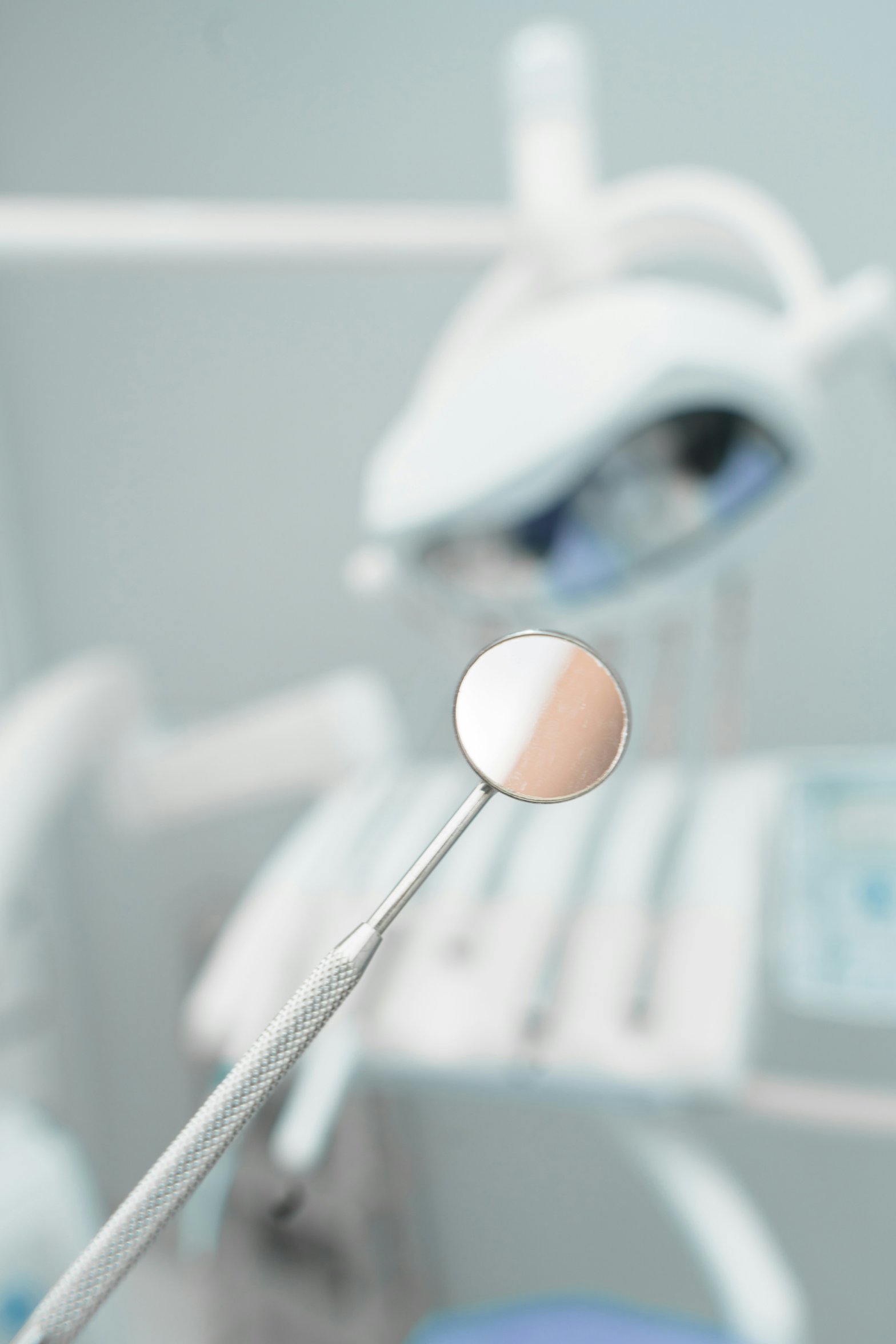 A dental mirror held in front of a blurred dental chair